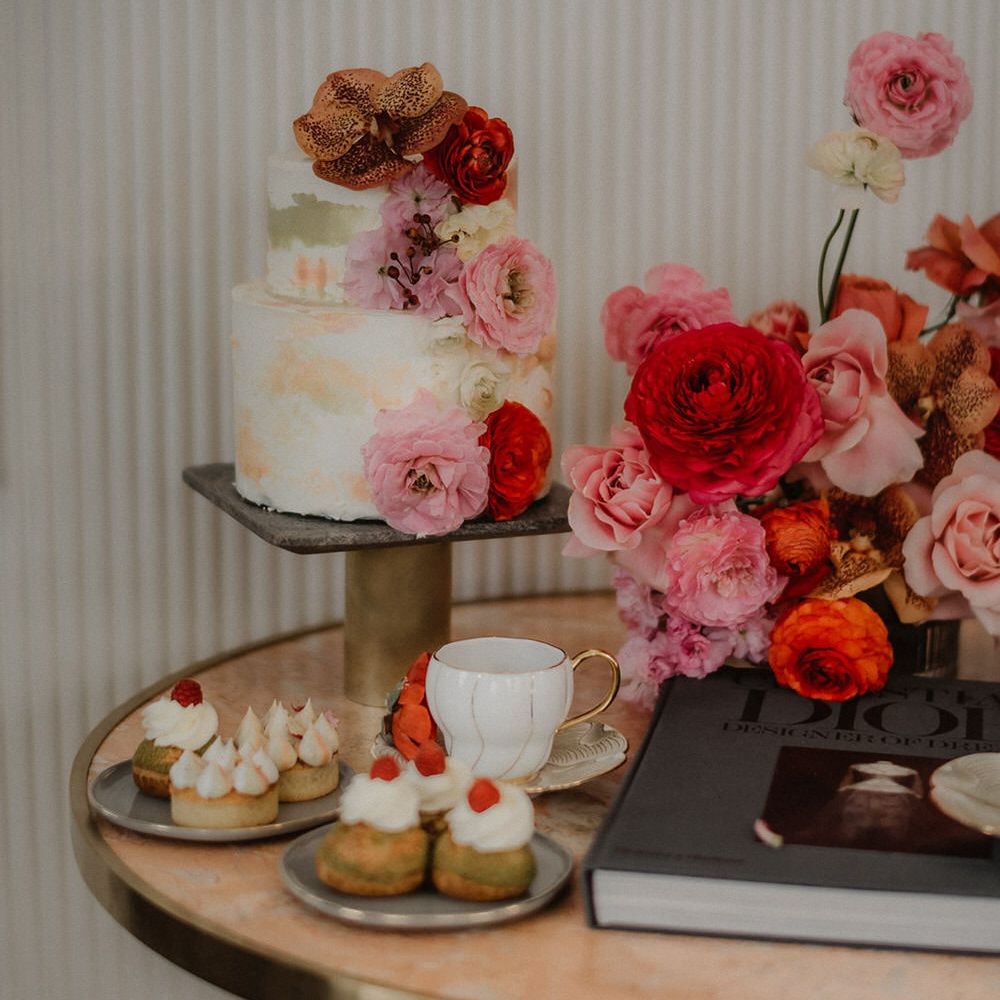 Two tier wedding cake with pastel colour brush effect detail and pink and peach wedding flower decoration, with afternoon tea and treats