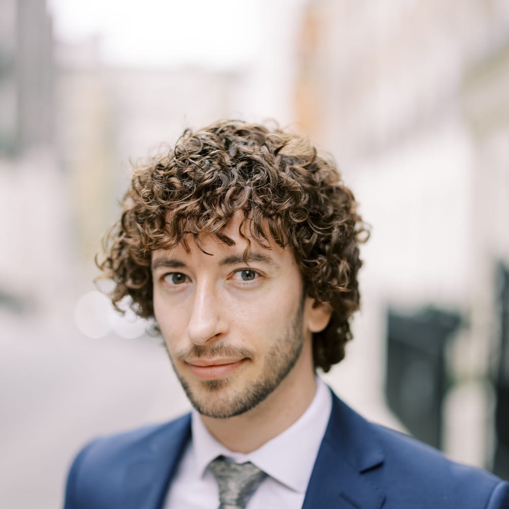 Groom looks toward camera whilst wearing blue suit and grey tie 