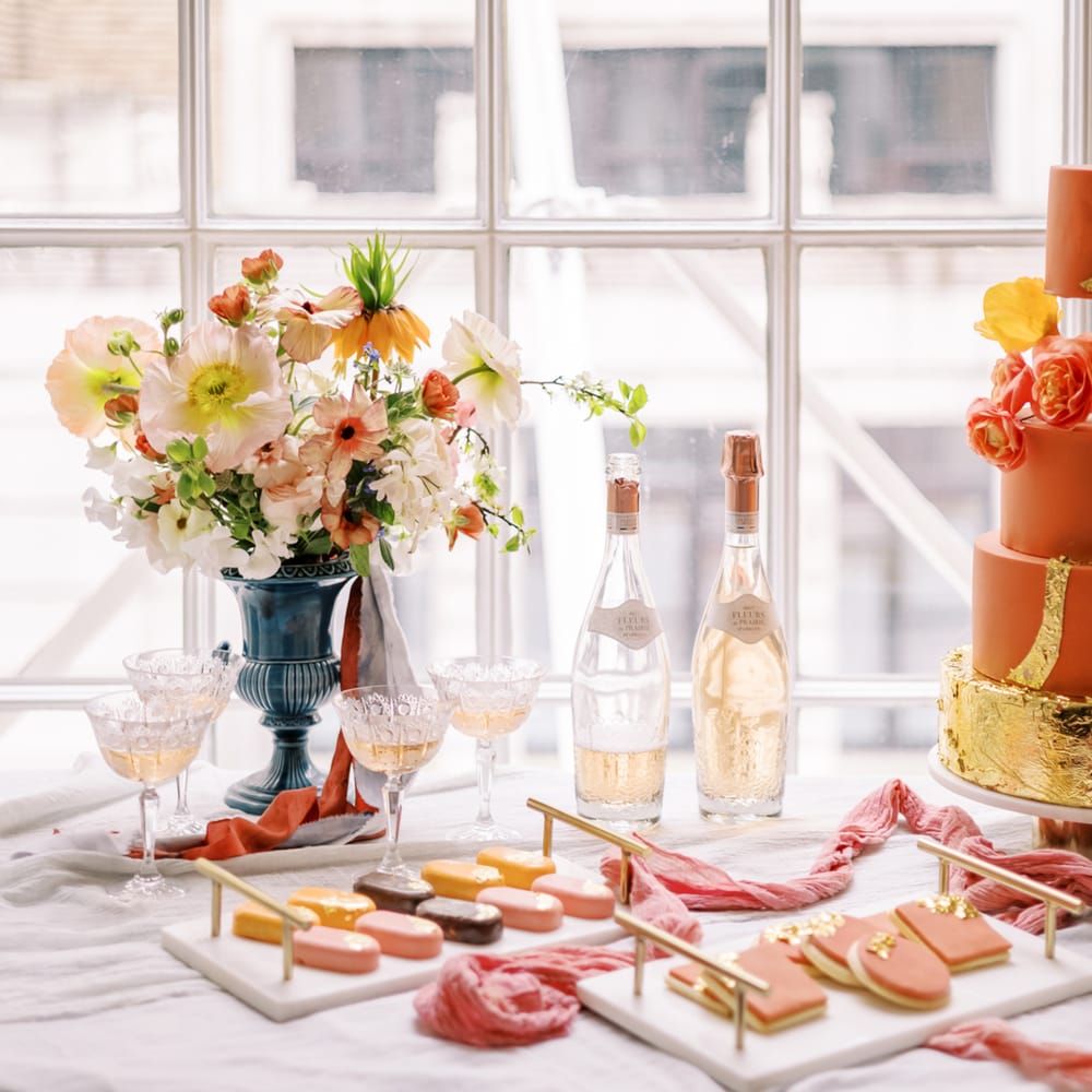 Orange wedding cake on white table cloth next to floral display and dessert favours in pastel colours