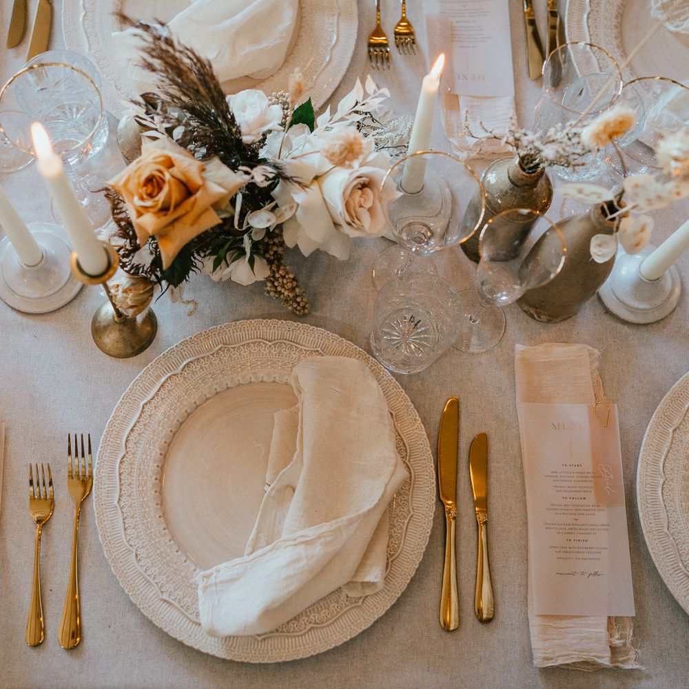 Place setting with ornate tableware, linen napkin and flower stems in cases 