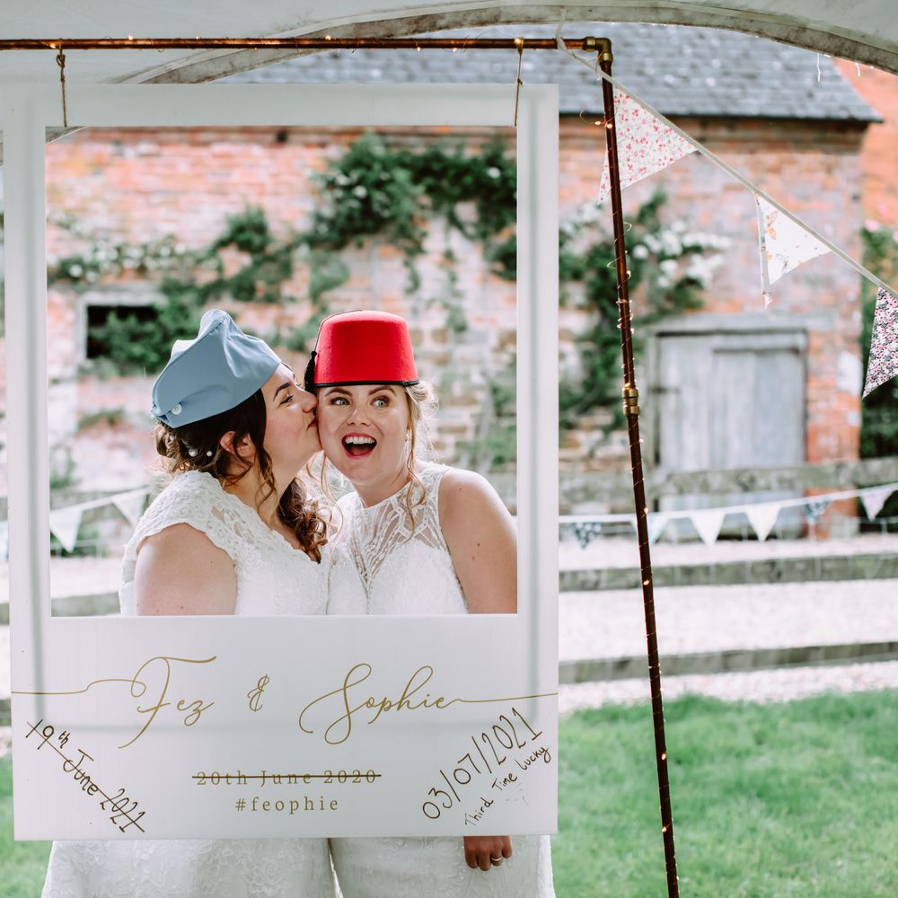 Bride kisses her bride on the cheek as they wear hats outdoors on their wedding day