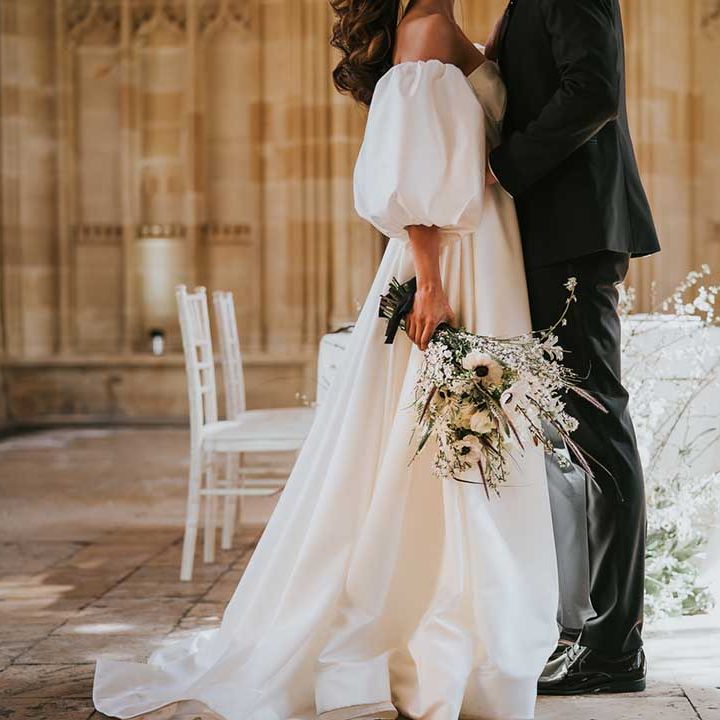 Bride in a full skirt wedding dress with detachable puff sleeve holding a white wedding bouquet with anemones 