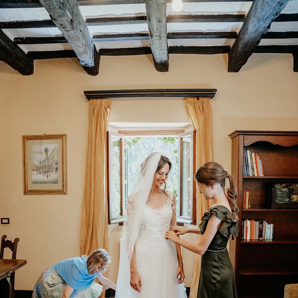 Bridesmaid wearing deep green silk dress helps bride get ready on the morning of her wedding day | Royal Studio
