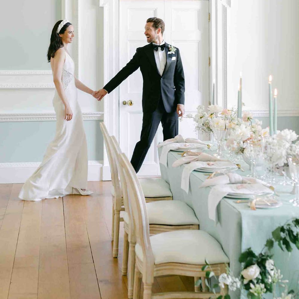 Groom in a tuxedo escorting his bride in a fitted wedding dress to their pale green wedding reception at Botley's Mansion