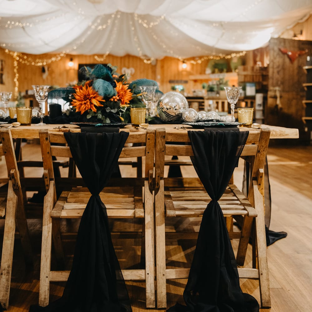 Rustic wedding reception with wooden tables and chairs, blue and orange flowers and fairy lights