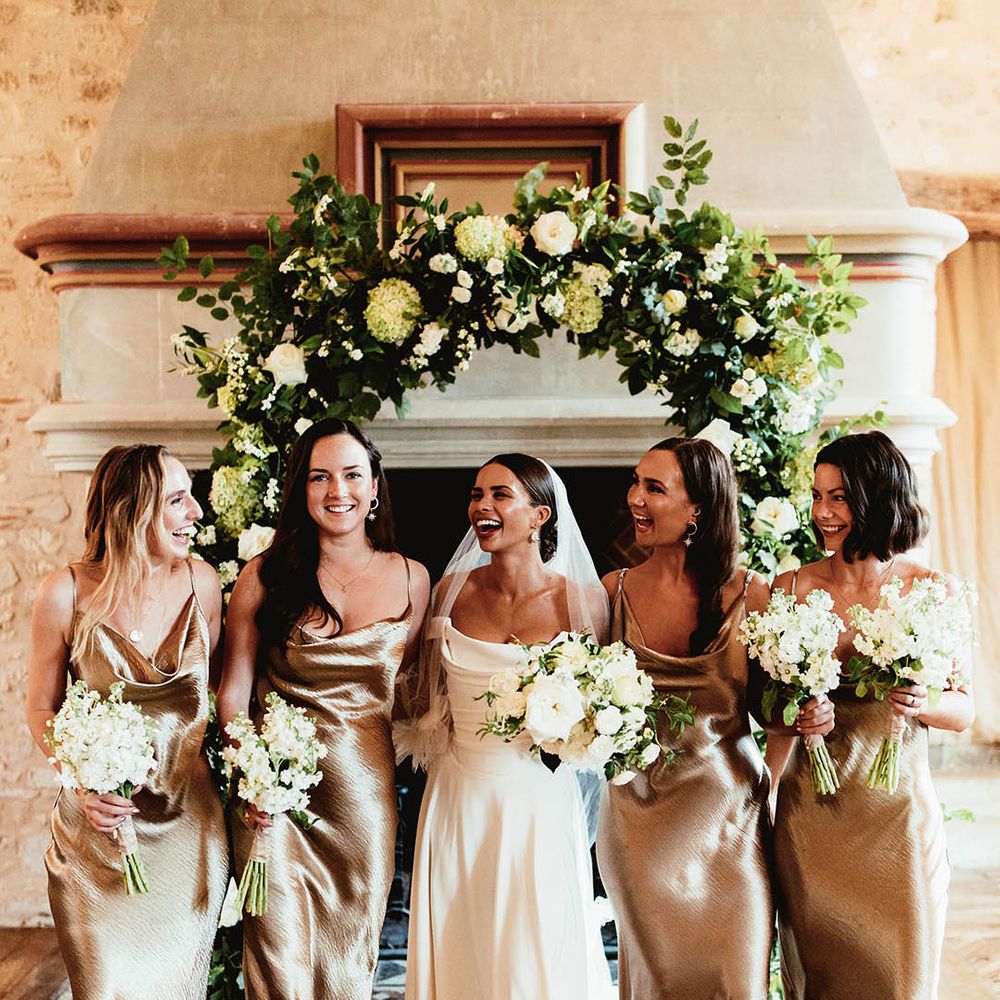 Bride stands with her bridesmaids who wear gold satin dresses with straps
