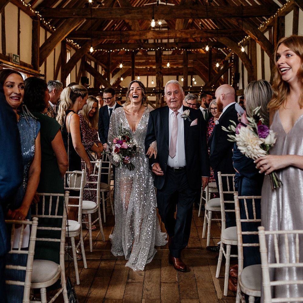 Tithe Barn, Loseley House wedding ceremony with Father of the bride in a navy suit walking his daughter down the aisle in a grey coloured wedding dress