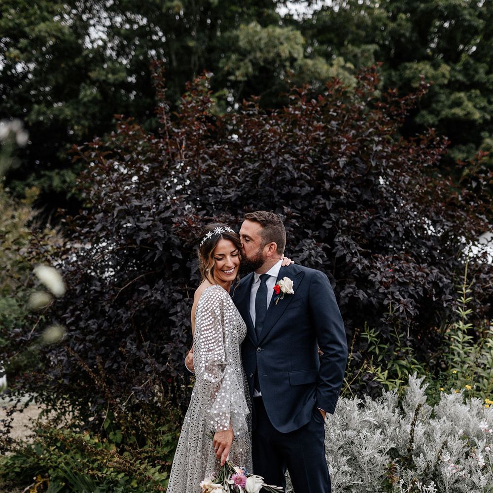 Groom in a navy suit embracing his bride in a silver sequin wedding dress at tipi wedding 