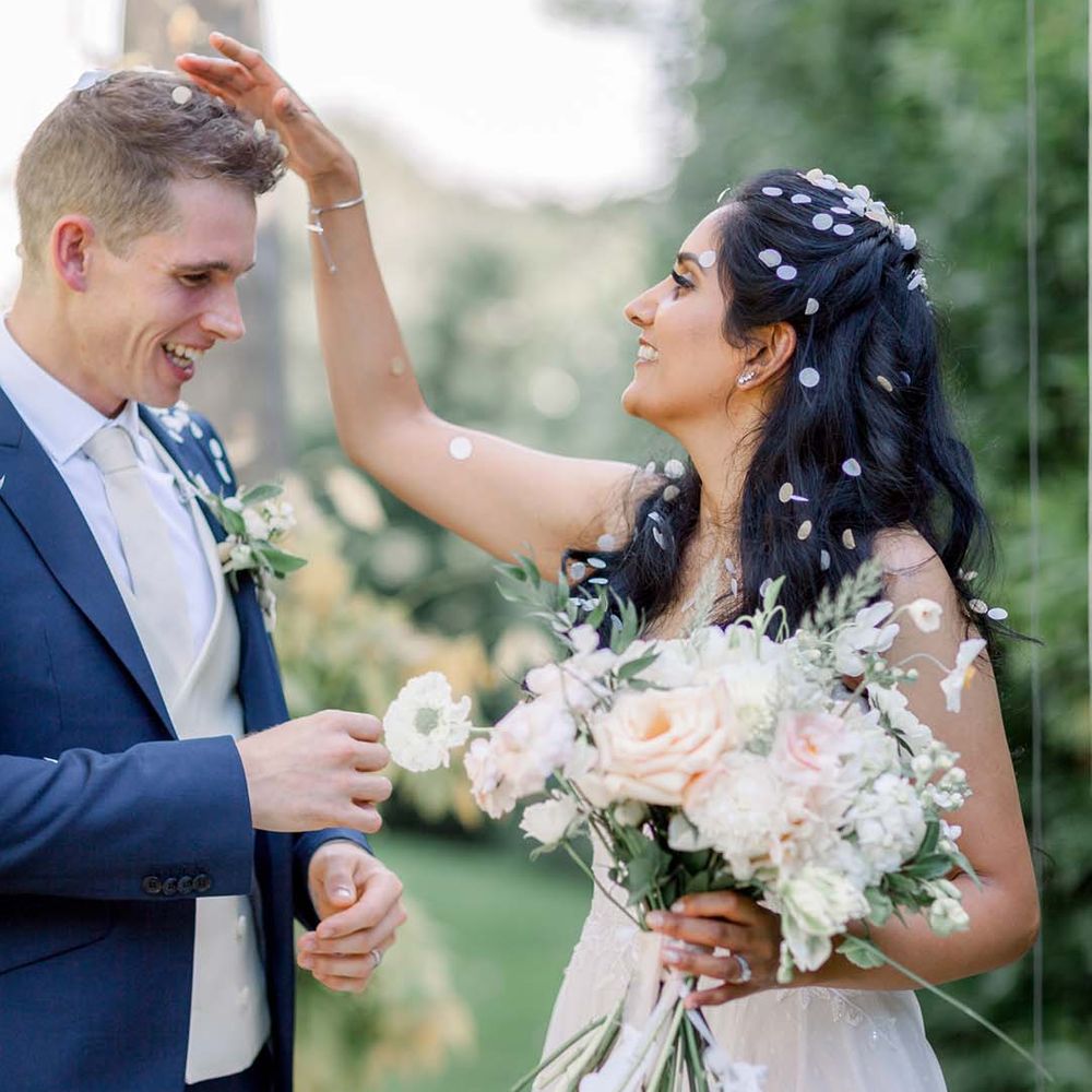 Bride & groom laugh whilst covered in confetti outdoors on their wedding day