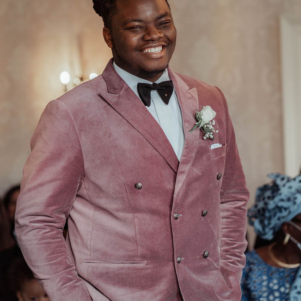 Groom wears dusky pink jacket for wedding complete with floral buttonhole and black tie 