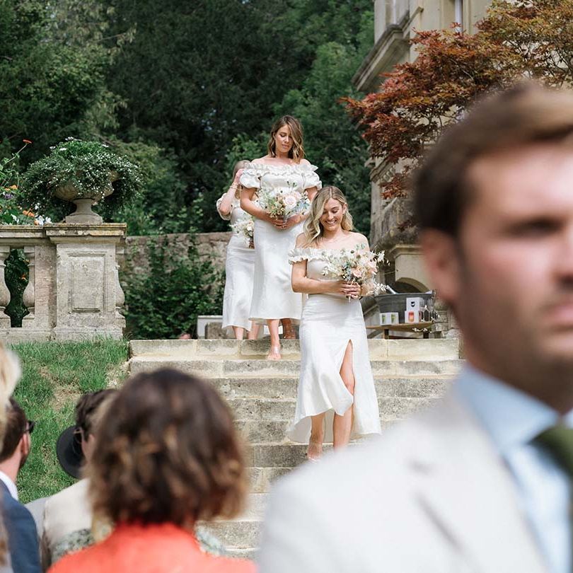 Bridesmaids approach the aisle in their white off the shoulder Bardot style dresses