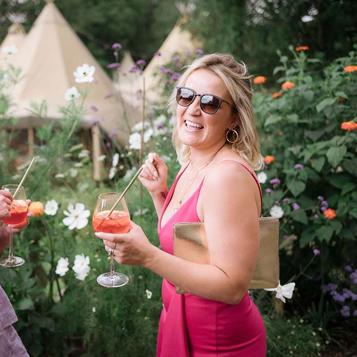 Wedding guest in lilac patterned dress and guest in bright pink dress with aperol spritz's in hand for garden wedding