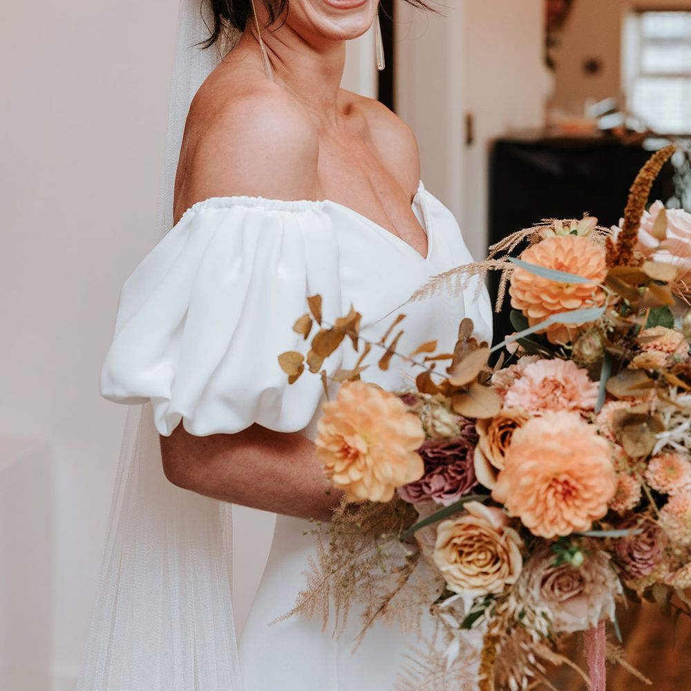 Bride in puff sleeve Alexandra Grecco dress with neutrala utumnal wedding bouquet and dangly earrings