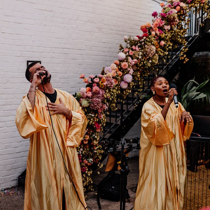 Flash mob choir singing at industrial London wedding venue with a staircase decorated in wedding flowers behind them 