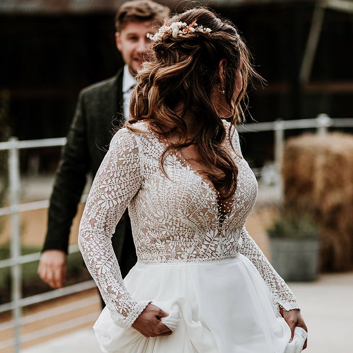 Bride in sheer lace and long sleeve v neck top looking back at groom in dark green suit