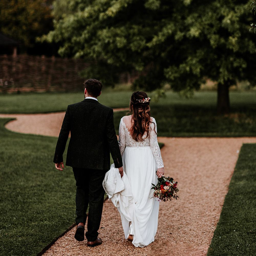 Bride with half up half down hair walks holding hands with groom and her orange wedding bouquet