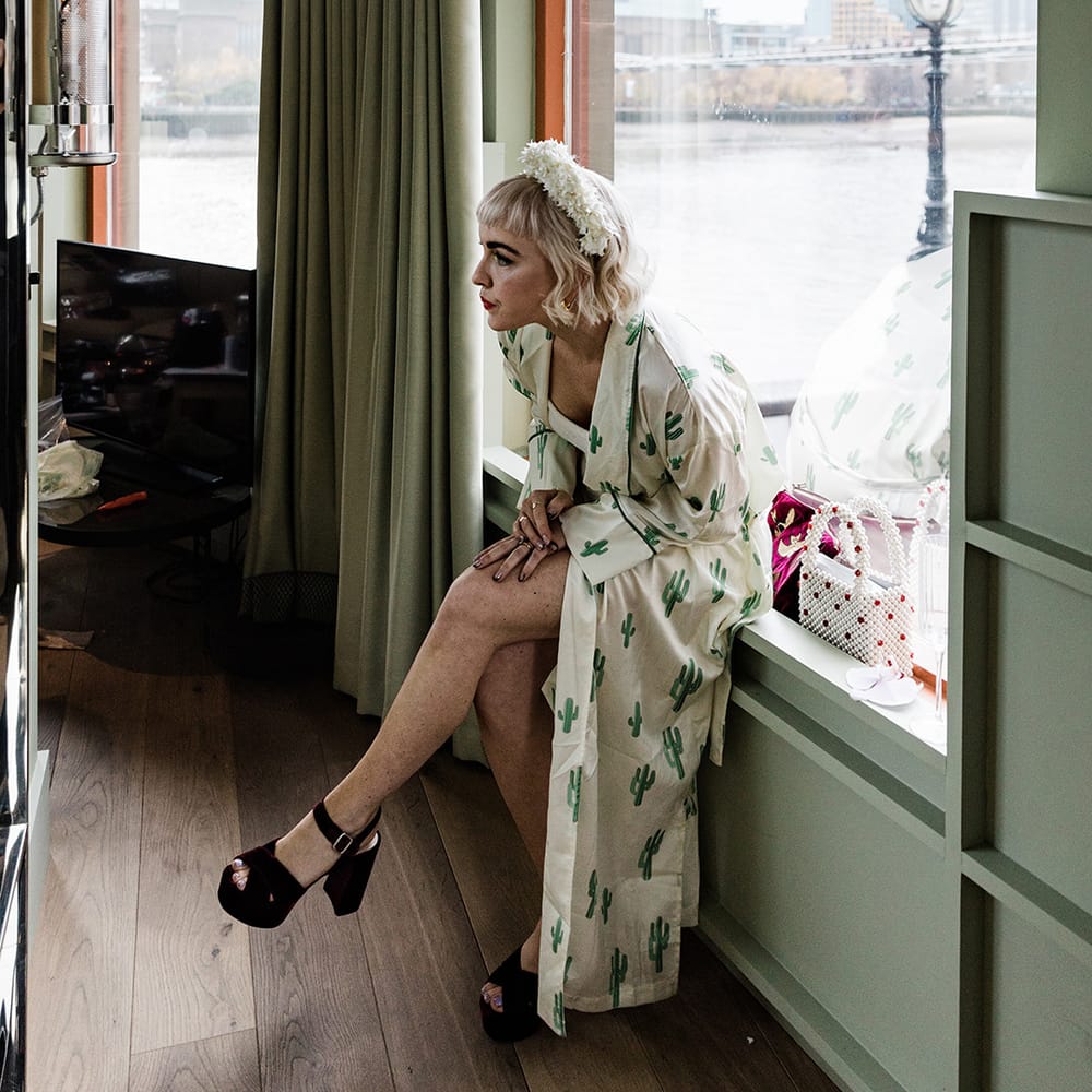 Bride in platform block heel wedding shoes and cactus print robe with white flower headband as she gets ready for her day 