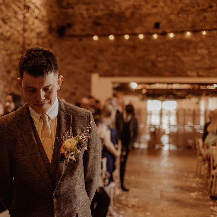 Groom in three piece brown suit waits at the altar for the bride to walk down with best man next to him 