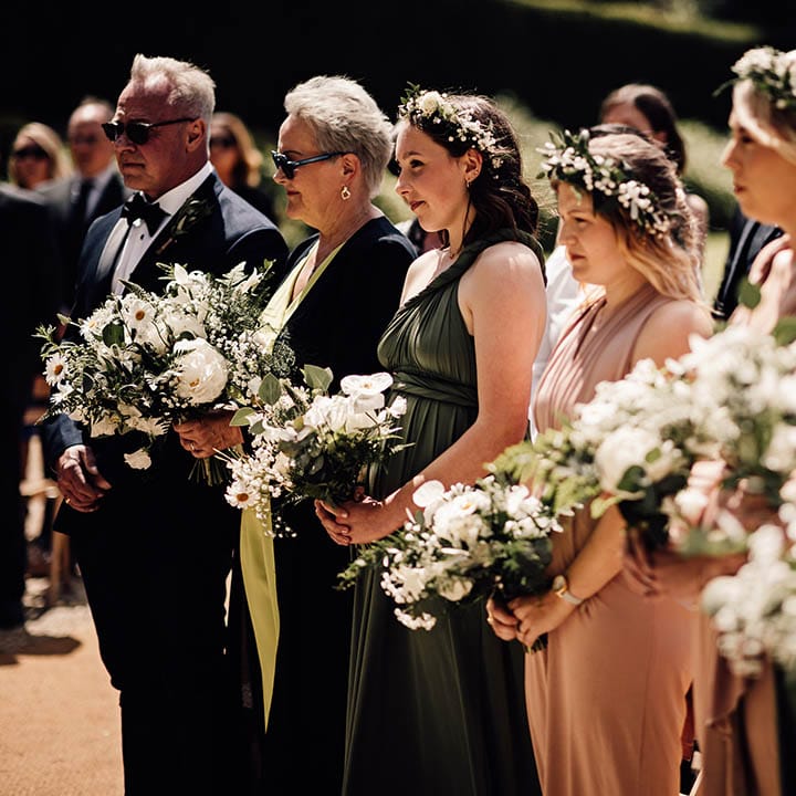 Bridesmaids in pale pink and olive green bridesmaid dresses with white flower crowns and white flower bouquets