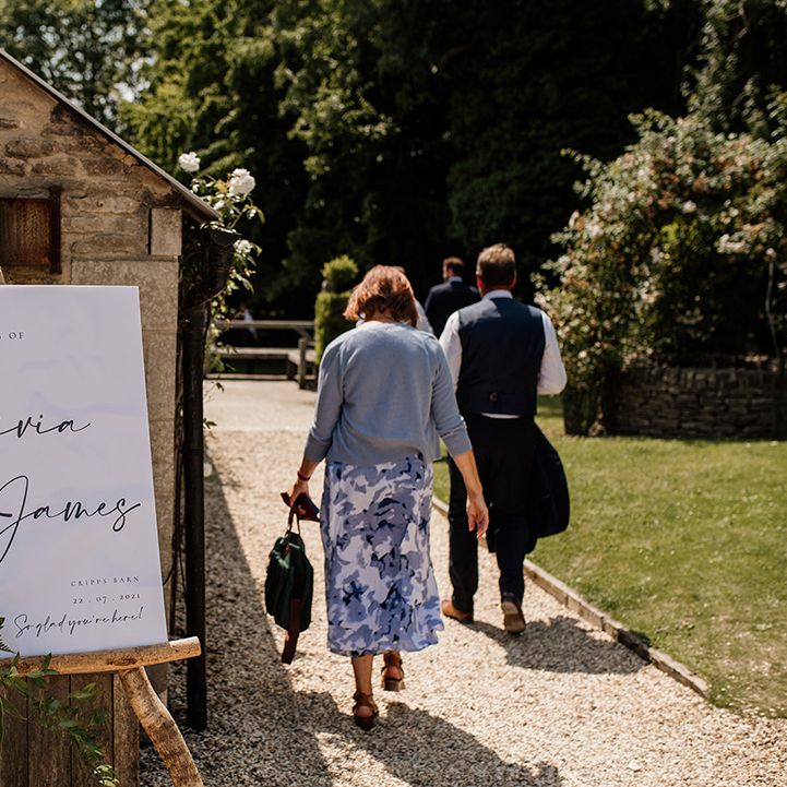 Black and white wedding welcome sign on wooden easel with white flower arrangement 