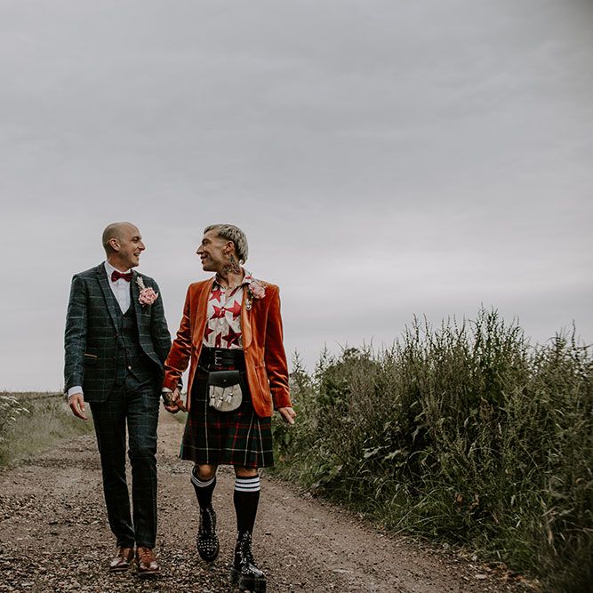 Grooms stand in the road wearing tartan suit and kilt complete with orange blazer and red bow tie 
