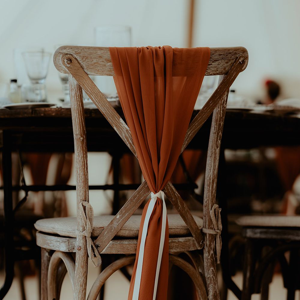 Chair back decorated with sheer orange fabric and white tie 