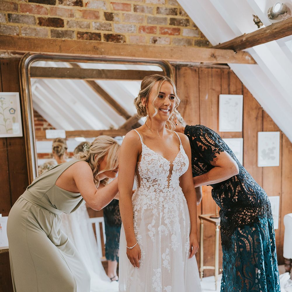 Bridesmaid and mother of the bride helps the bride into her lace wedding dress and finishing touches for the big day