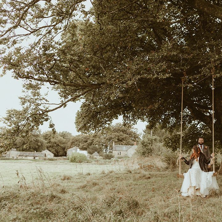 Groom in grey tweed wedding suit with the bride sitting on the large swing at Trevenna Barns wedding venue in Cornwall 