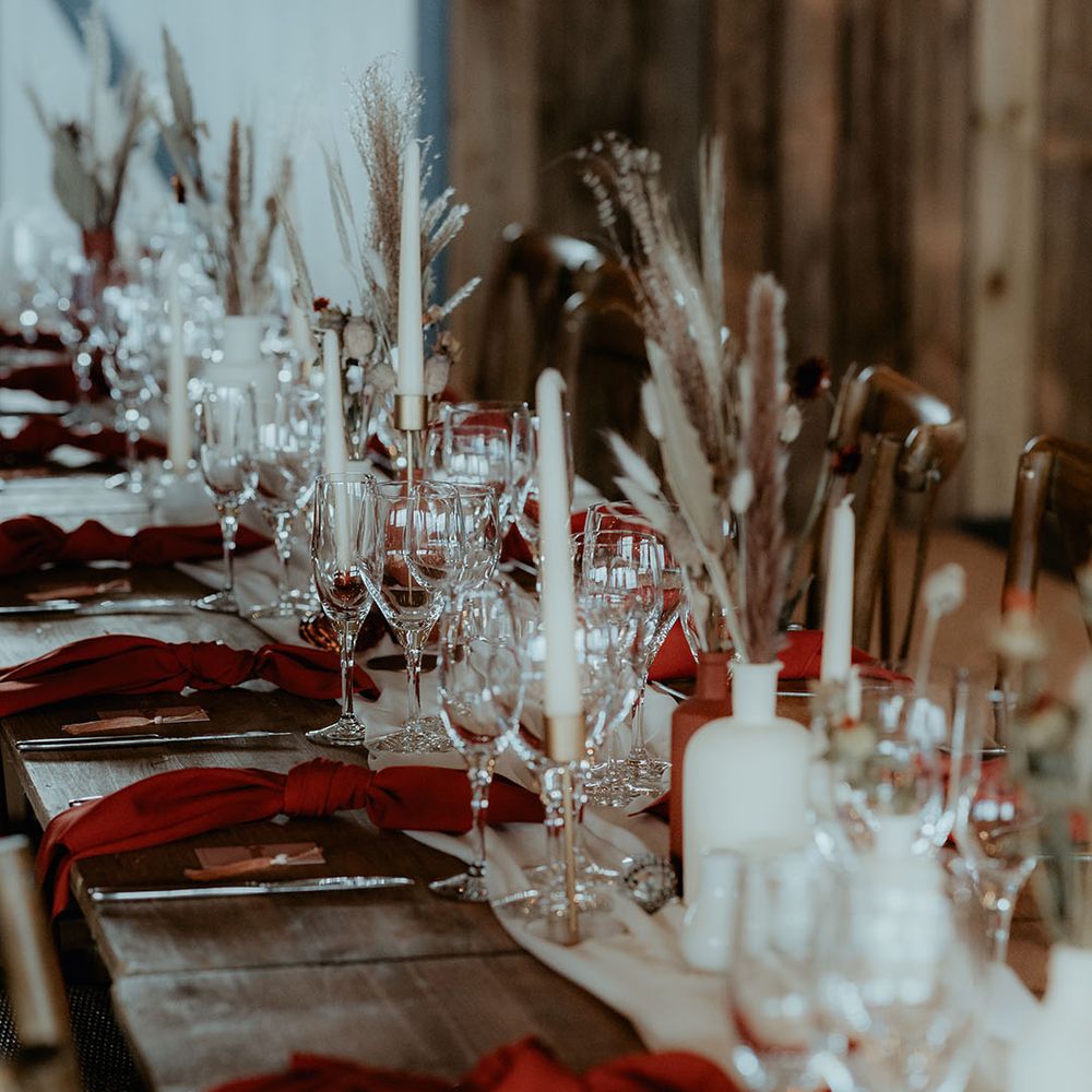 Wooden banquet table with white table runner and white candles with burnt orange napkins and bunny grass decor 