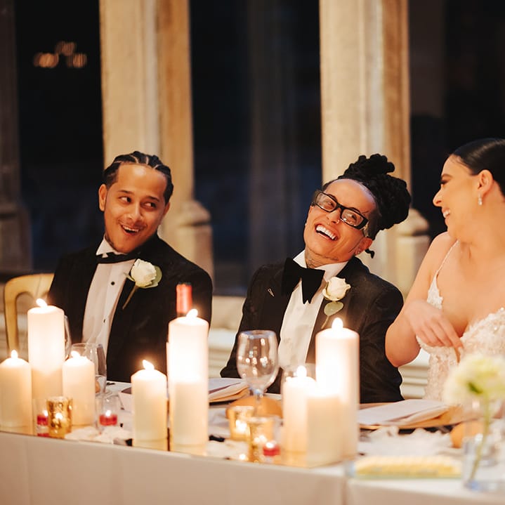 Bride in black snakeskin print tuxedo with black bowtie and white rose boutonniere laughing with bride in lace sleeveless v neck Enzoani wedding dress during wedding speeches at Grittleton House
