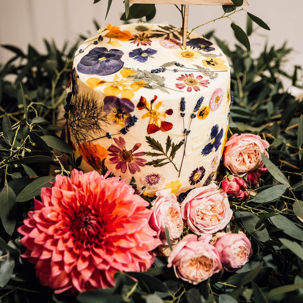 Single tier buttercream iced wedding cake with pressed wildflowers and personalised cake topper 