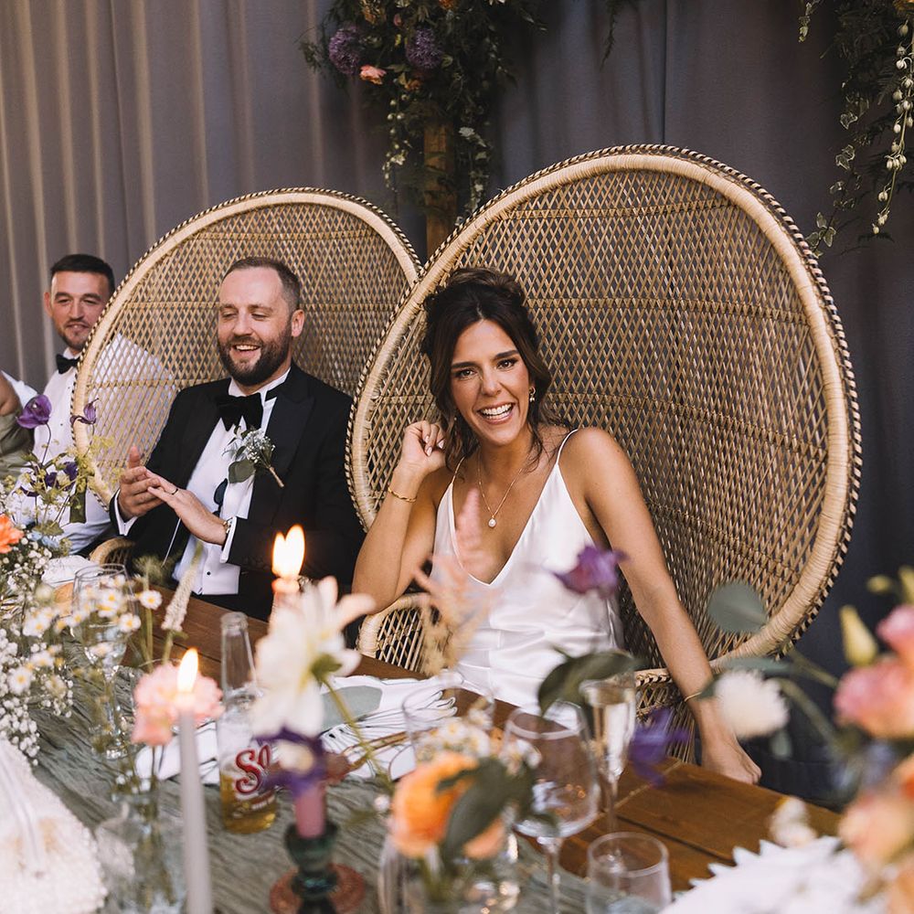 The bride and groom is on peacock chairs at their wedding breakfast on the top table 