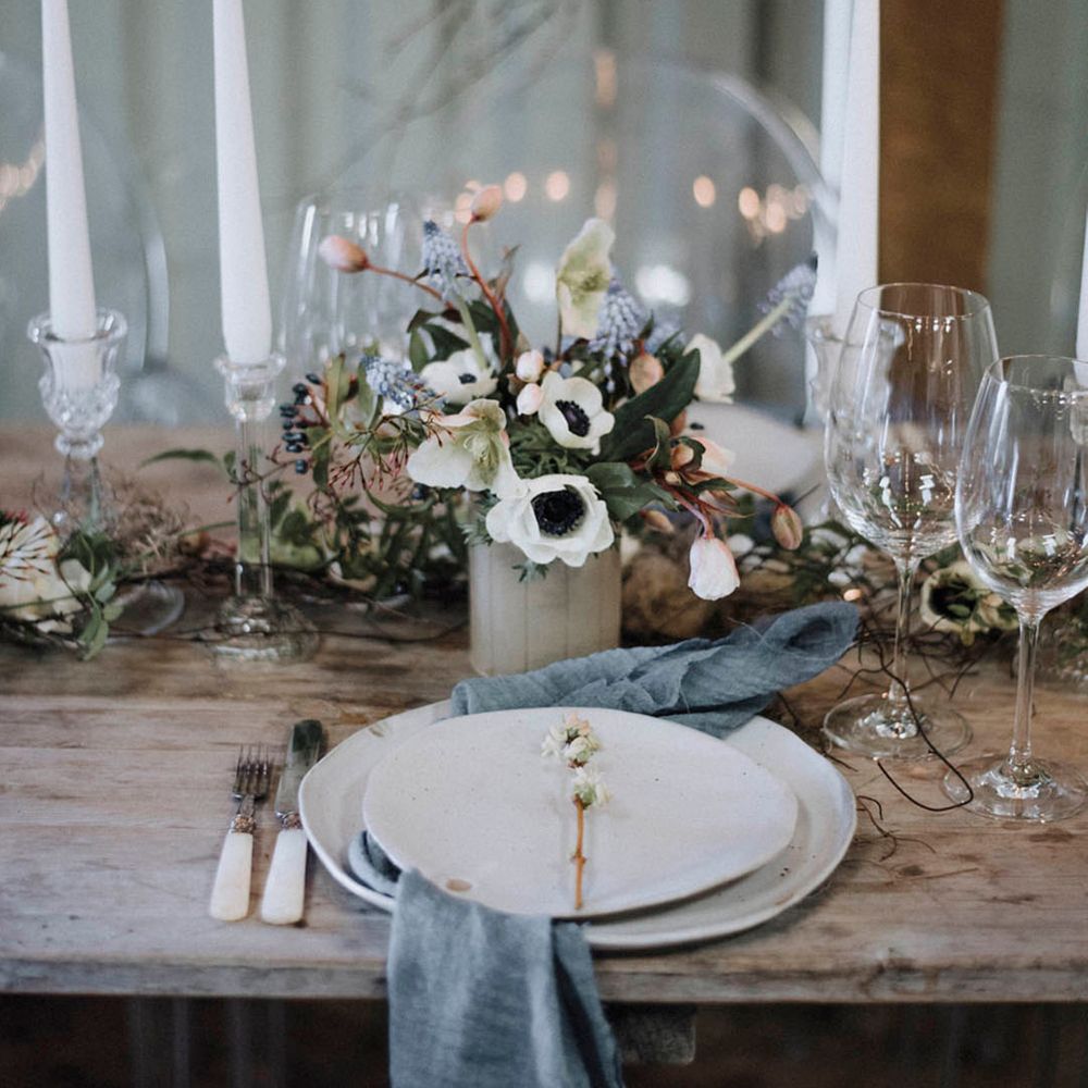 White wedding plates with blue napkins with white taper candles with wedding flower arrangements 