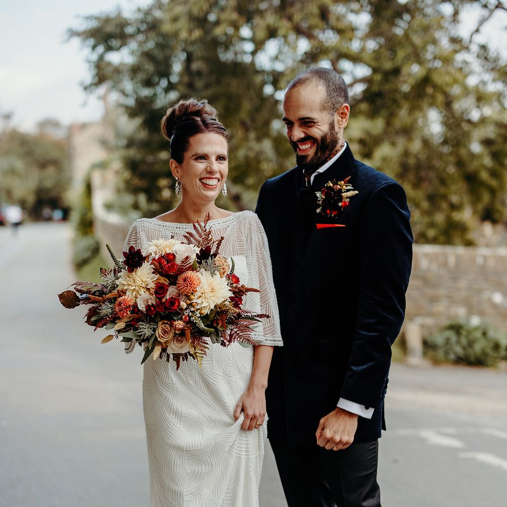 Bride & groom stand together outdoors carrying floral bouquet 