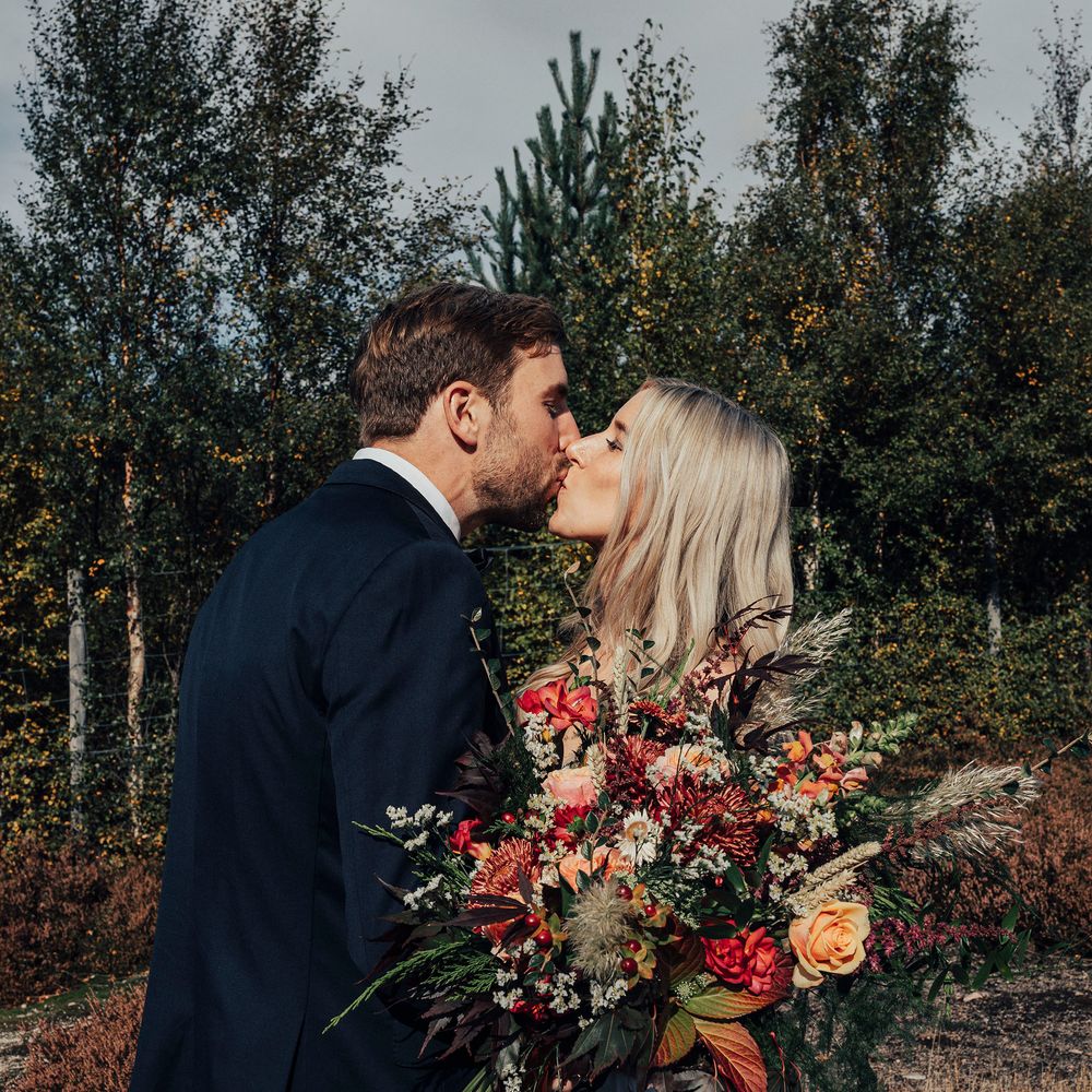 Bride & groom kiss in Scottish countryside whilst she holds floral bouquet 