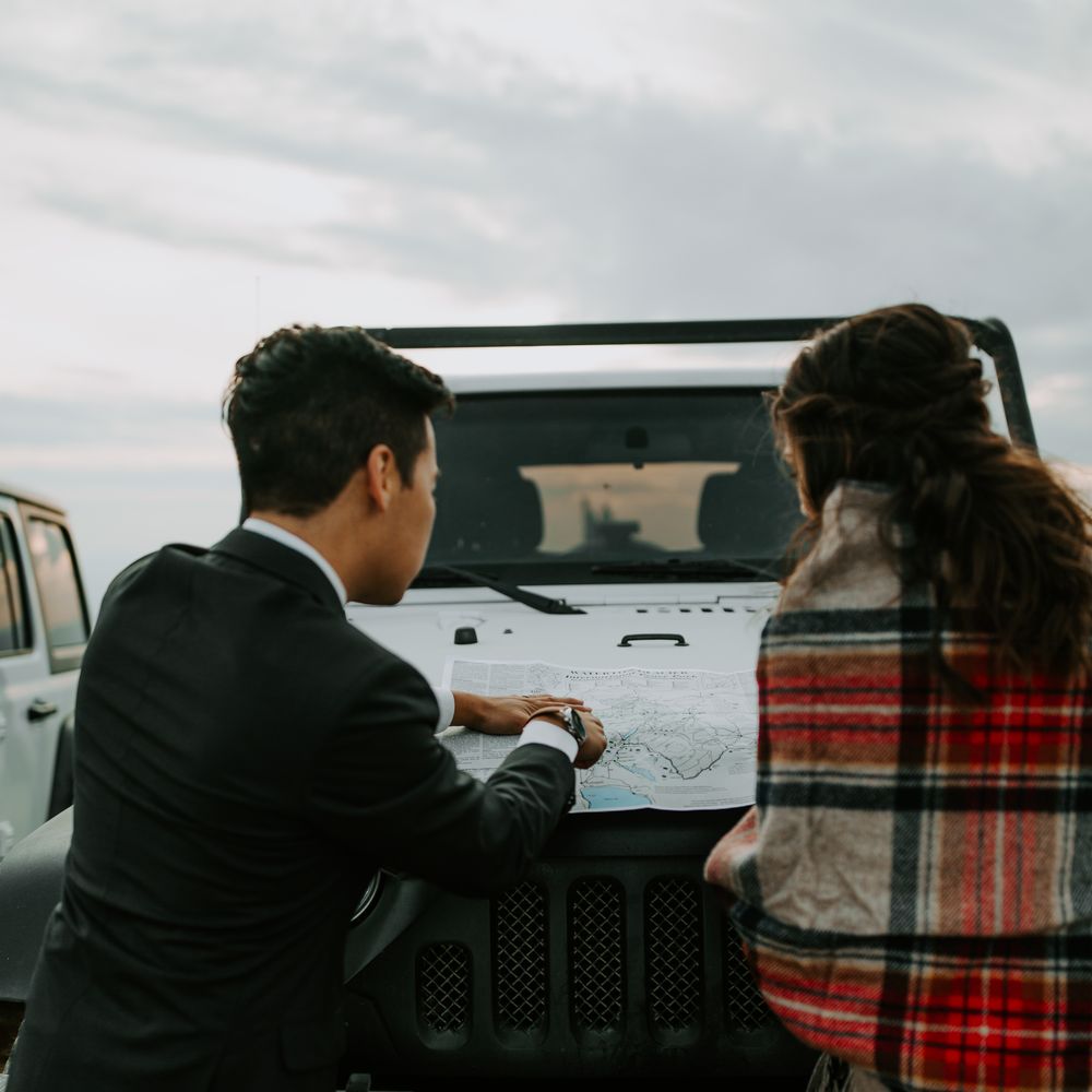 Bride & groom look at map on the bonnet of white Jeep