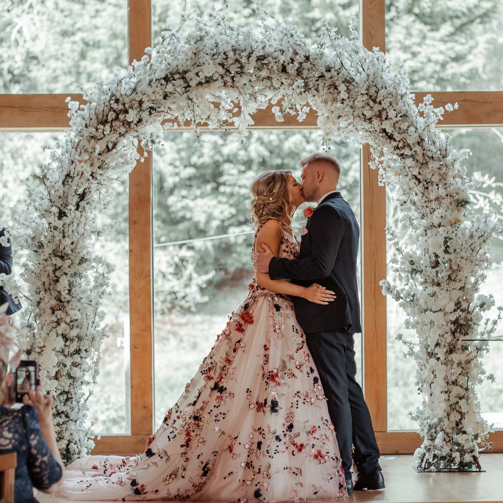 Bride & groom kiss beneath floral archway on their wedding day