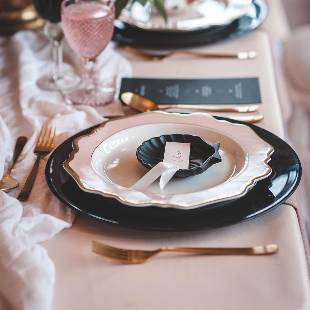 Place setting with black and gold rimmed tableware, and an ornate shell plate 