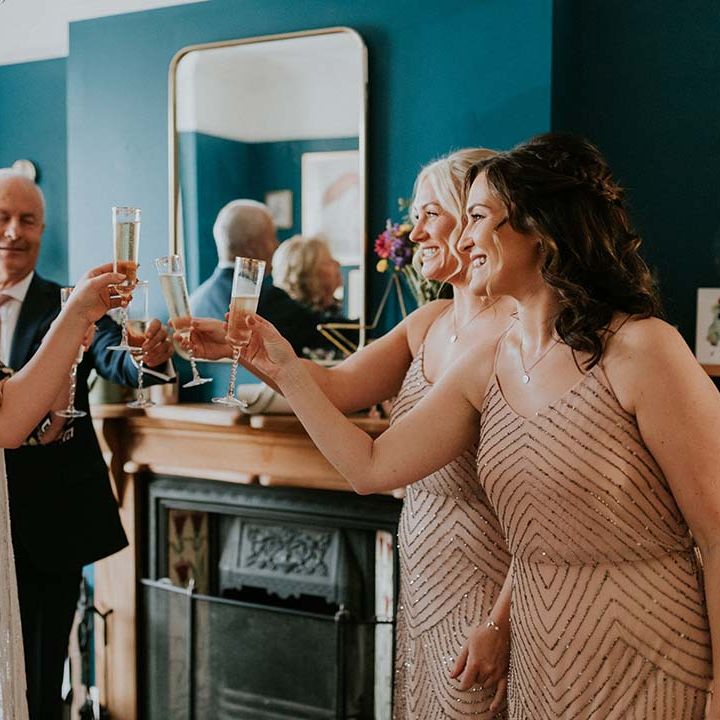 Bride raises a glass with her bridesmaids on wedding day who wear sparkling dresses