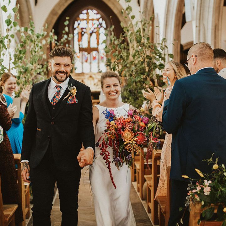Church wedding ceremony with groom in a navy suit and floral tie and bride in a Charlie Brear Wedding dress with vibrant wedding bouquet 