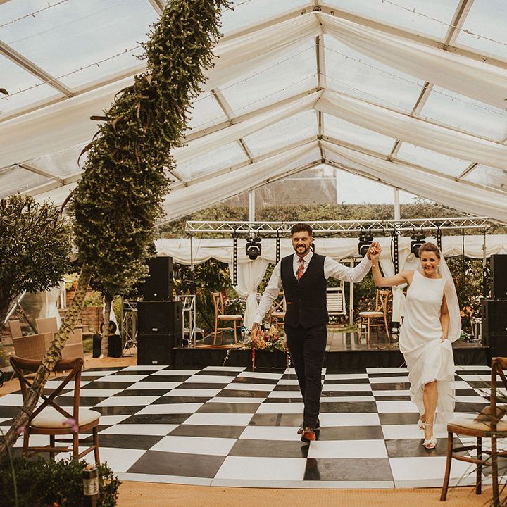 Bride and groom entering their back garden clear marquee wedding reception across the black and white dance floor 