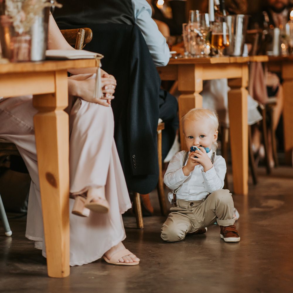 Young wedding guest in white shirt and braces plays with toy at rustic barn wedding reception