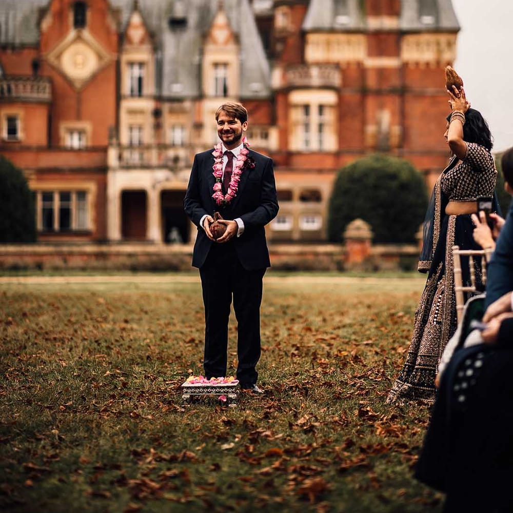 Groom wears dark suit with burgundy tie and pink flowers at Minley Manor 