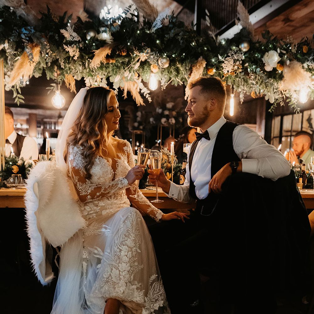 Bride and groom toast to each other with fur throws on the chairs for winter Christmas wedding 