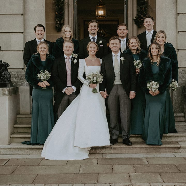 Wedding party, bride in Suzanne Neville long wedding dress, bridesmaids in bottle green Suzanne Neville long bridesmaids dresses and black cropped fur coats