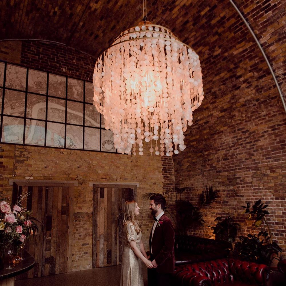Red leather sofa and modern chandelier decorate the bride and groom's wedding venue as they hold hands under the light 
