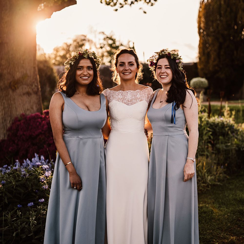 Bridesmaids in blue wedding dresses with flower crowns and bride in satin wedding dress with sheer lace long sleeves 