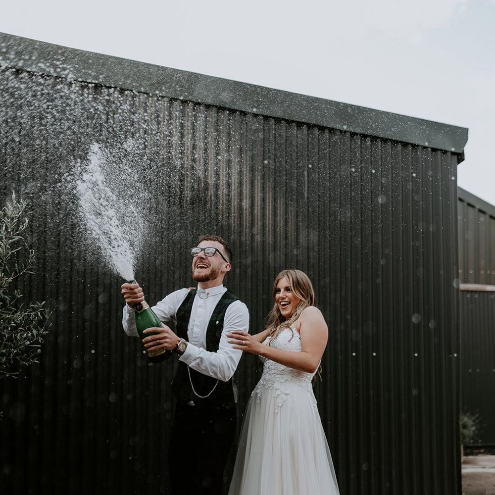 Bride in white strapless dress and groom doing champagne pop