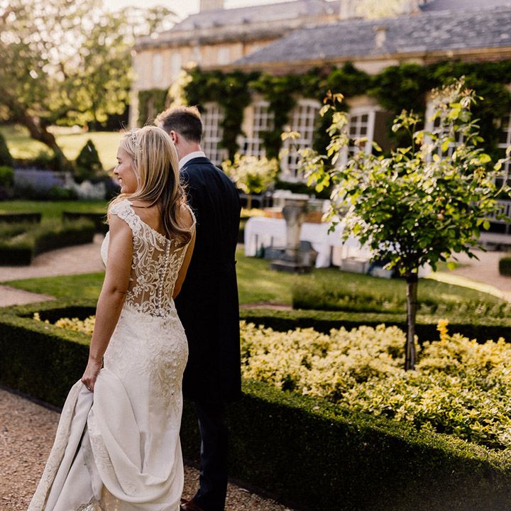 Bride in sheer lace back wedding dress with button detail walking around gardens at Goldney Hall with groom 