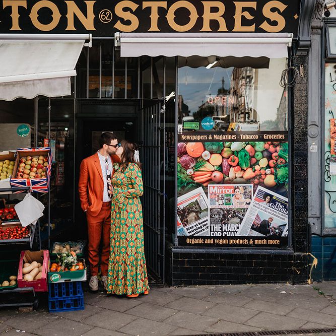 Bride & groom kiss in shop doorway on their wedding day in brightly coloured outfits 
